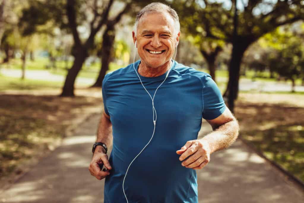 A smiling man doing a morning walk senior exercise routine in a park.