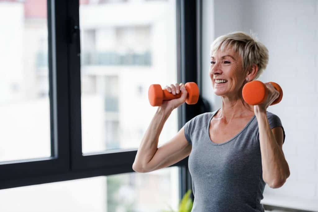 Senior exercise programs at home - a senior woman holding working out a home using dumbbells.