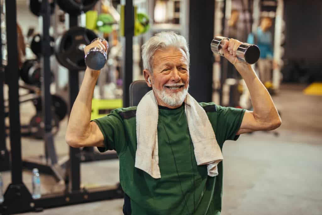Senior exercise fitness helping seniors 65 - a smiling senior man holding dumbbells at a gym.