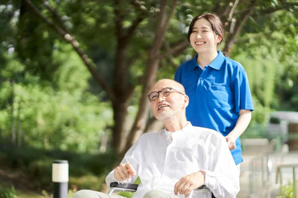 Caretaker fatigue - a smiling female caregiver supporting a senior man on a wheelchair.