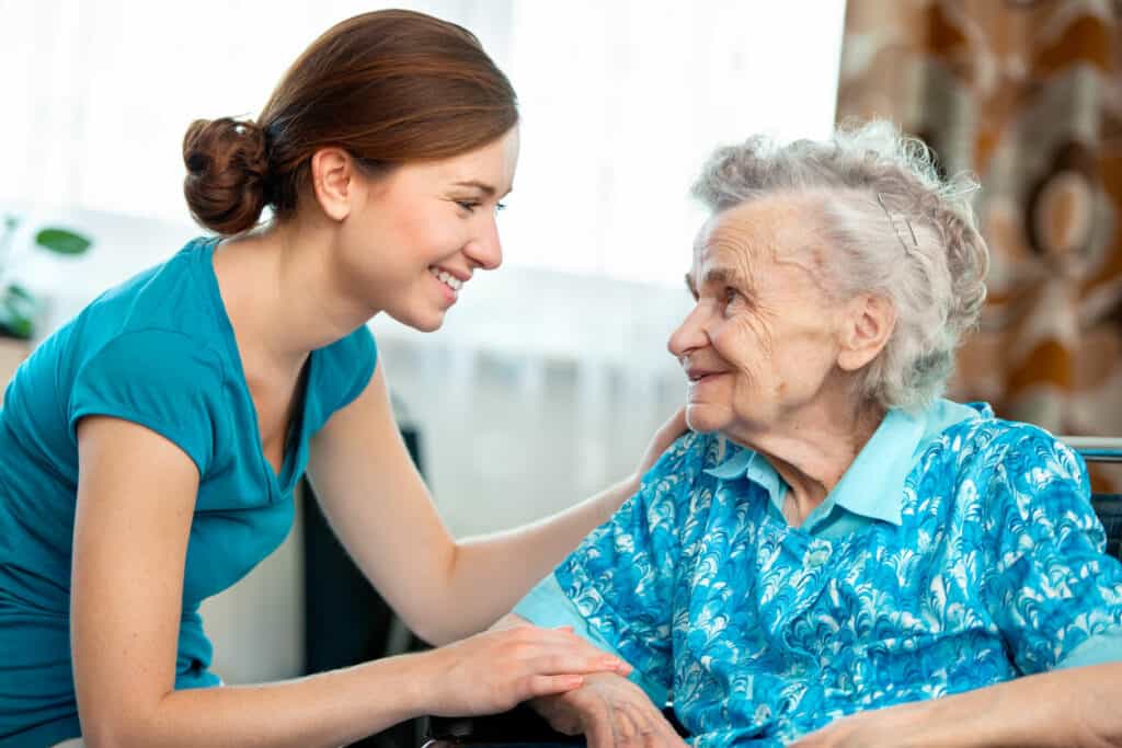 Caregiver syndrome - a young woman caregiver smiling at a senior woman.