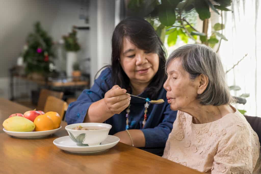 Asian daughter and caregiver feeding her elderly mother | Tips for caregivers of the elderly