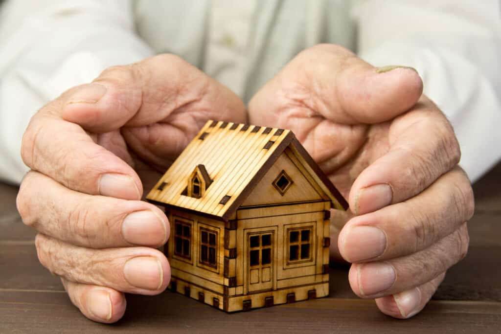 Hands of a senior surrounding a small wooden house | Advice for caregivers who want to provide the best attention