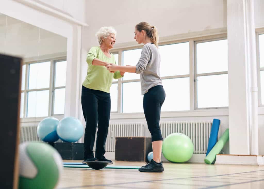 Physical therapist supporting elderly woman while doing balance training - home exercise for elderly