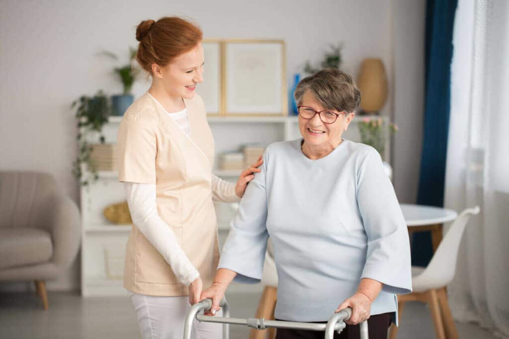 Medical expert caretaker helping a senior woman walk around. | A senior hotline can help you select the best caregiver for your aging loved one.