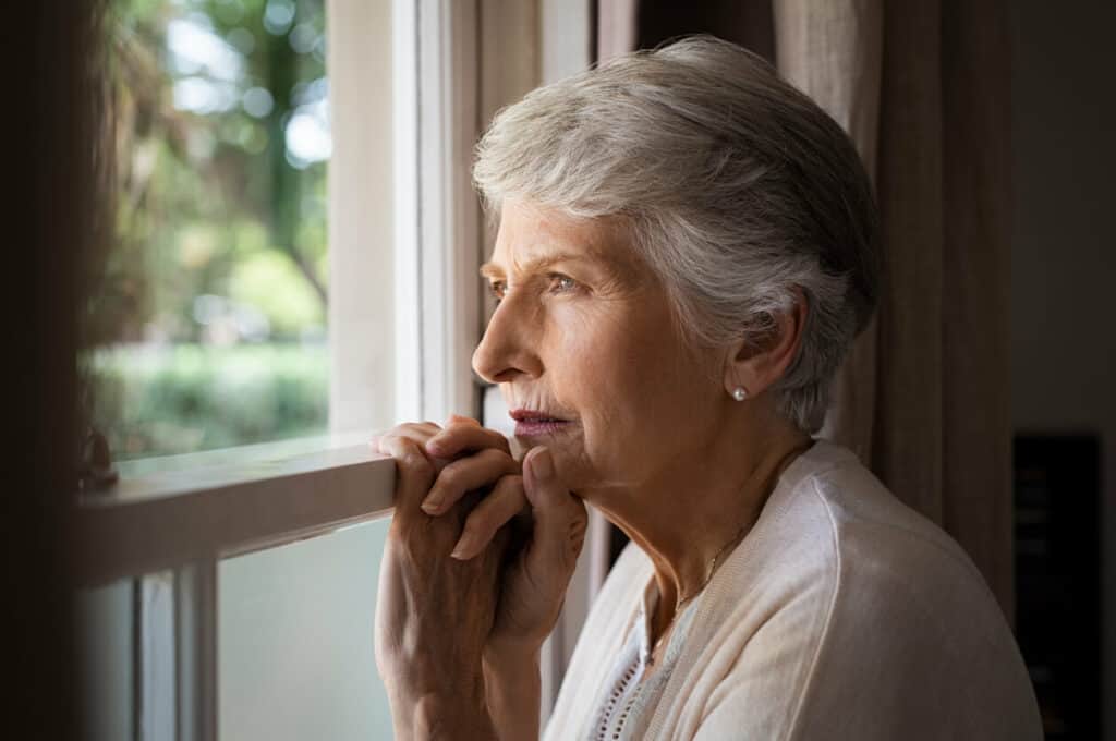 sad older woman looking through a window | caregiver depression