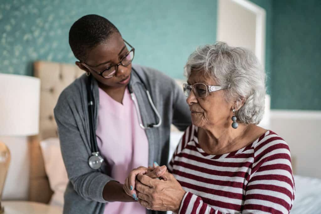 A mental health caregiver supporting an older woman in standing up.