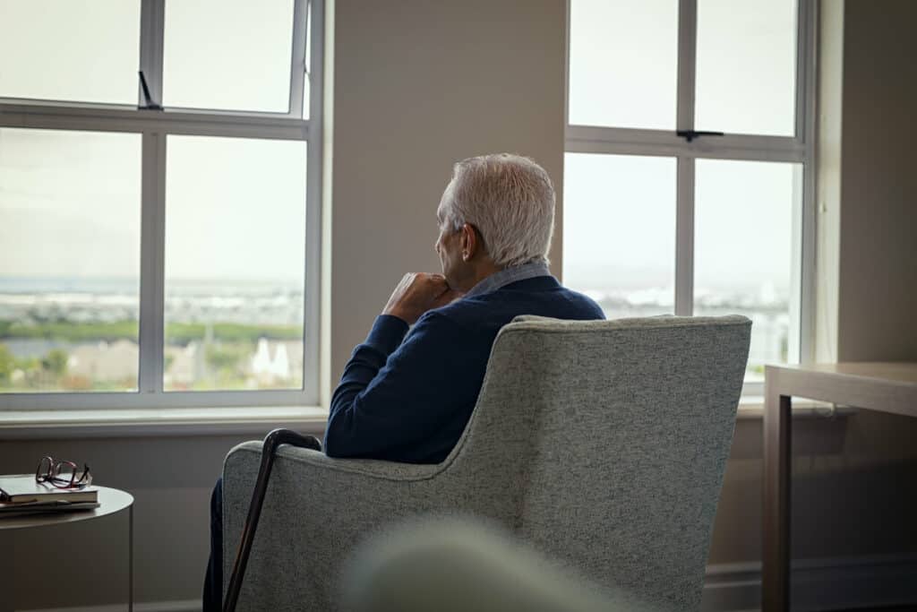 Caregiver mental health - a senior man looking out the window and feeling lonely.