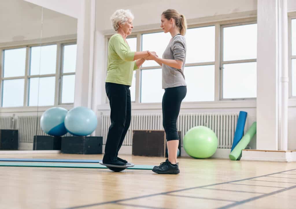 A female caregiver assisting an older woman standing on a bosu ball - balance exercise for older adults