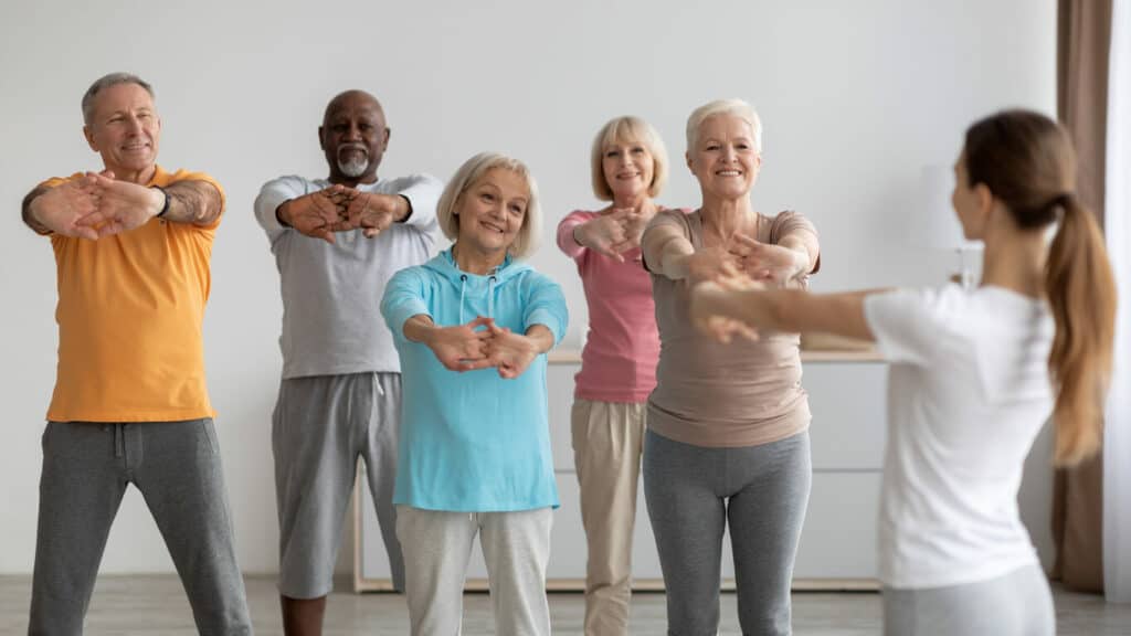 Group of elderly people taking a senior exercise class led by a caregiver