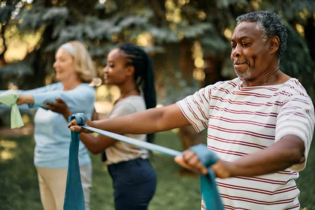 African American man with a senior exercise group stretching using a power band