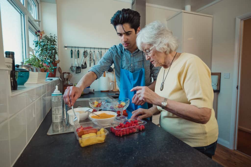 Young male caregiver making a healthy fruit compote with his female senior client