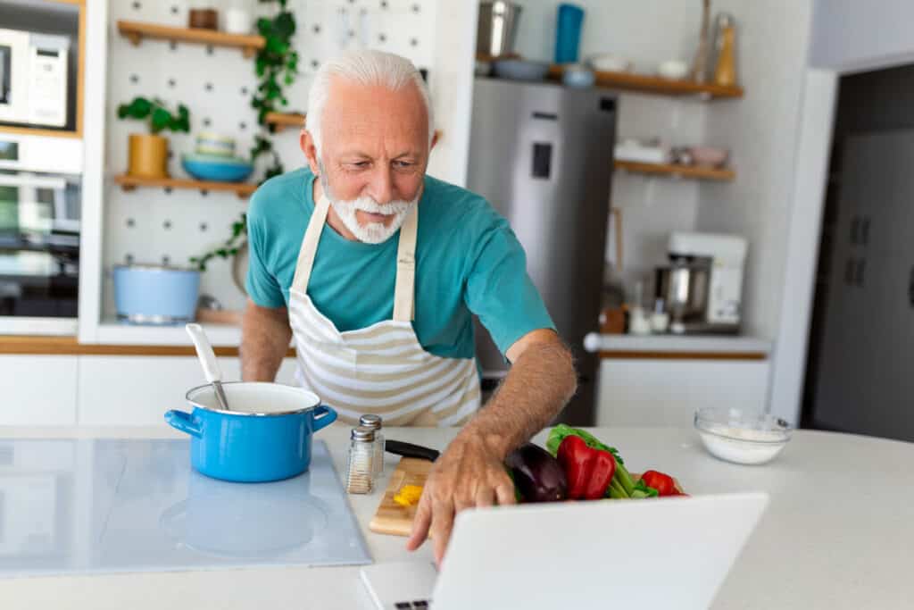 Aging male cooking a brain health meal by following a recipe on a computer screen