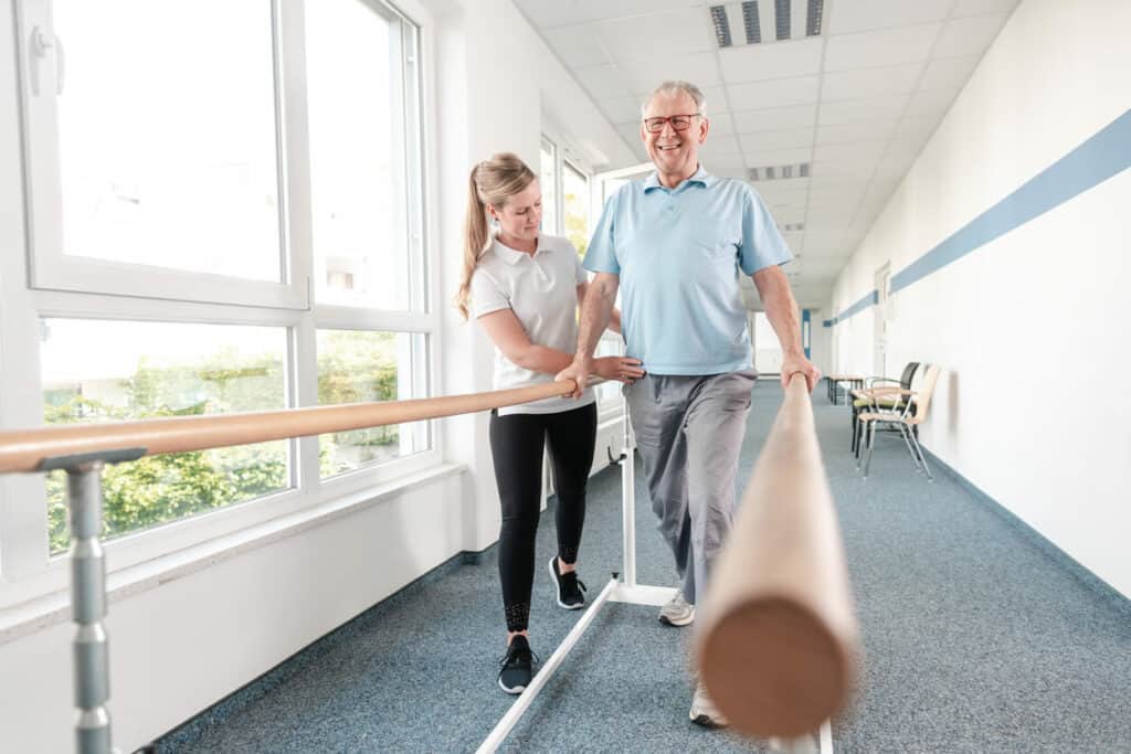 Elderly exercise benefits - a caregiver supporting a senior to do walking exercises.