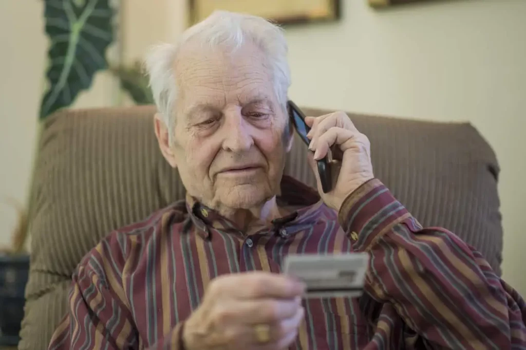 Stop scammers - a senior man talking to his phone while holding his credit card