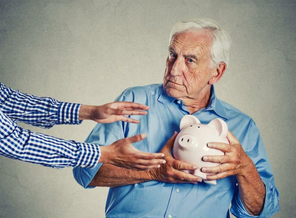 victims of scams - a senior holding a piggy bank while looking suspicious.