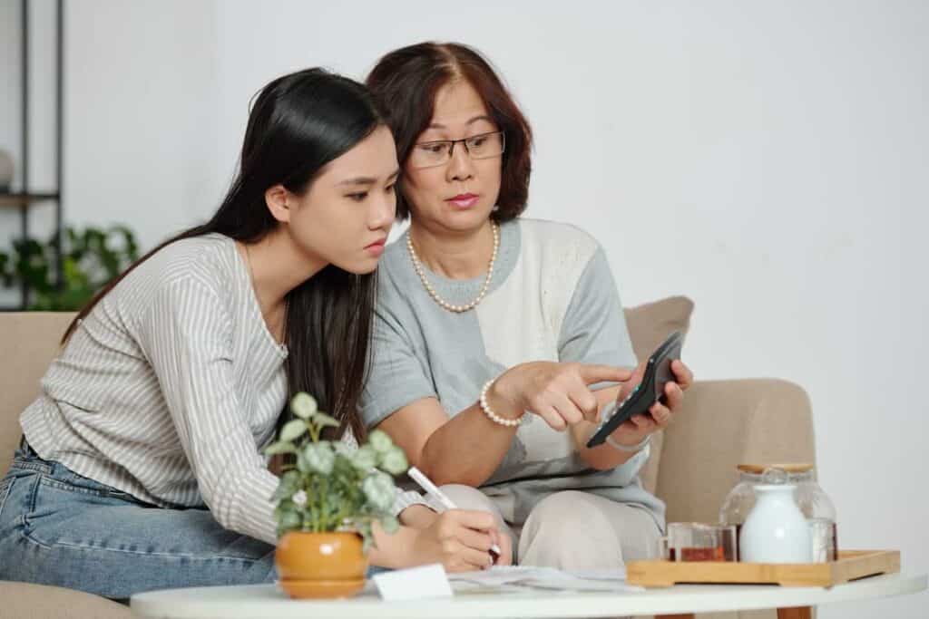 An elderly mother and young daughter doing calculations after the first lost money in an online scam