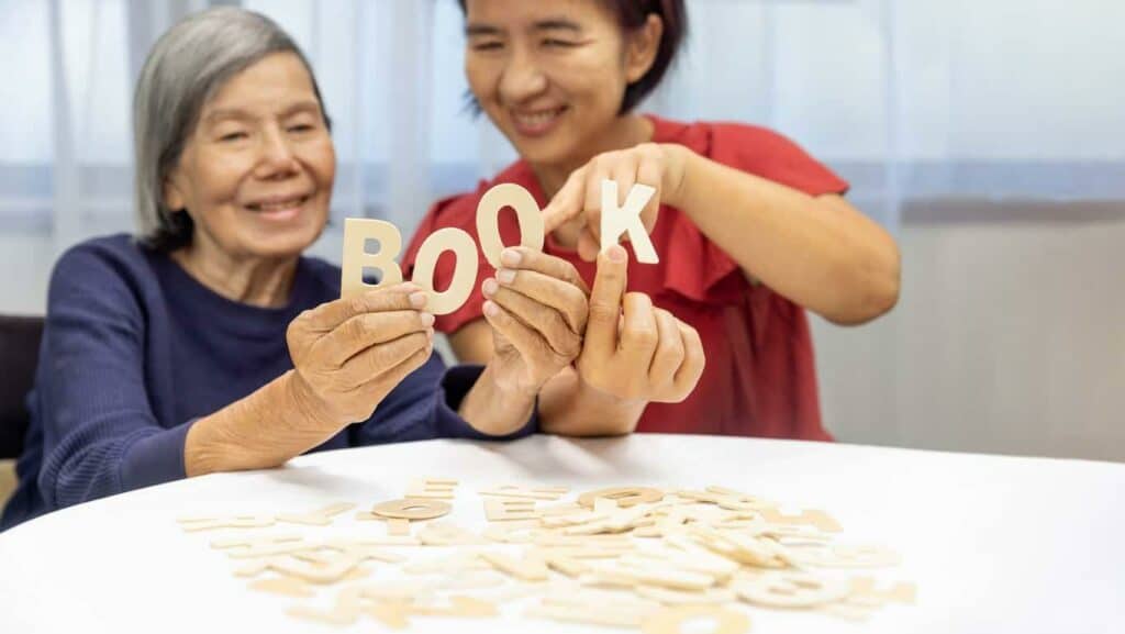 An older dementia patient playing alphabet games with caregiver to improve memory - patient teaching for dementia