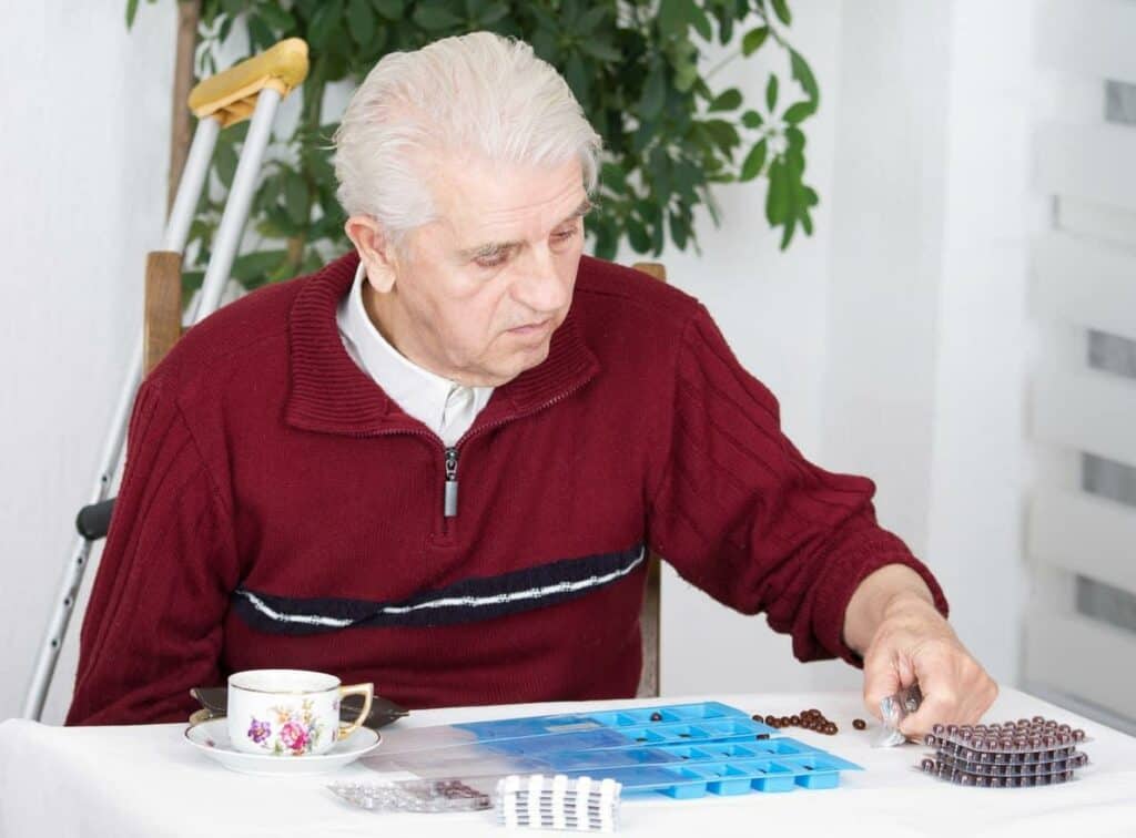 An older man learning to sort his medications in weekly pill container - dementia teaching