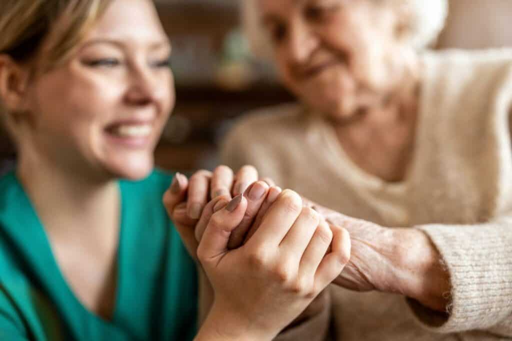 A senior woman with sundowner’s syndrome holding her caregiver’s hand.