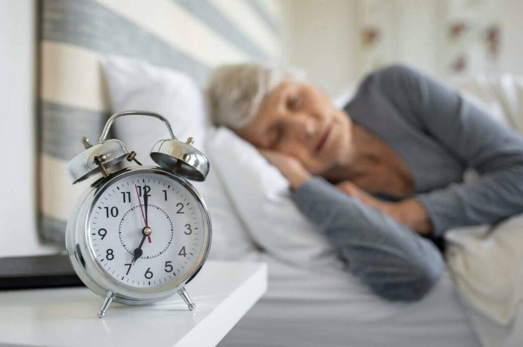 senior woman sleeping with an alarm clock on the side table - sundowning dementia treatment