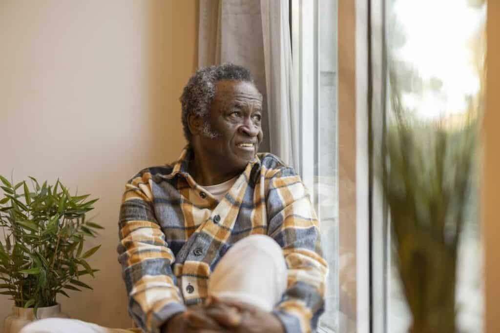 Black senior man looking outside and feeling confused, which is one of several common sundowning behaviors