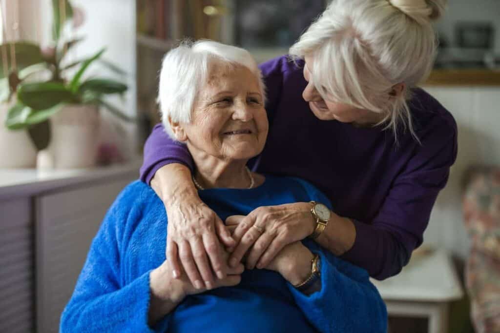 dementia stages - a senior woman with dementia hugged by a family caregiver.