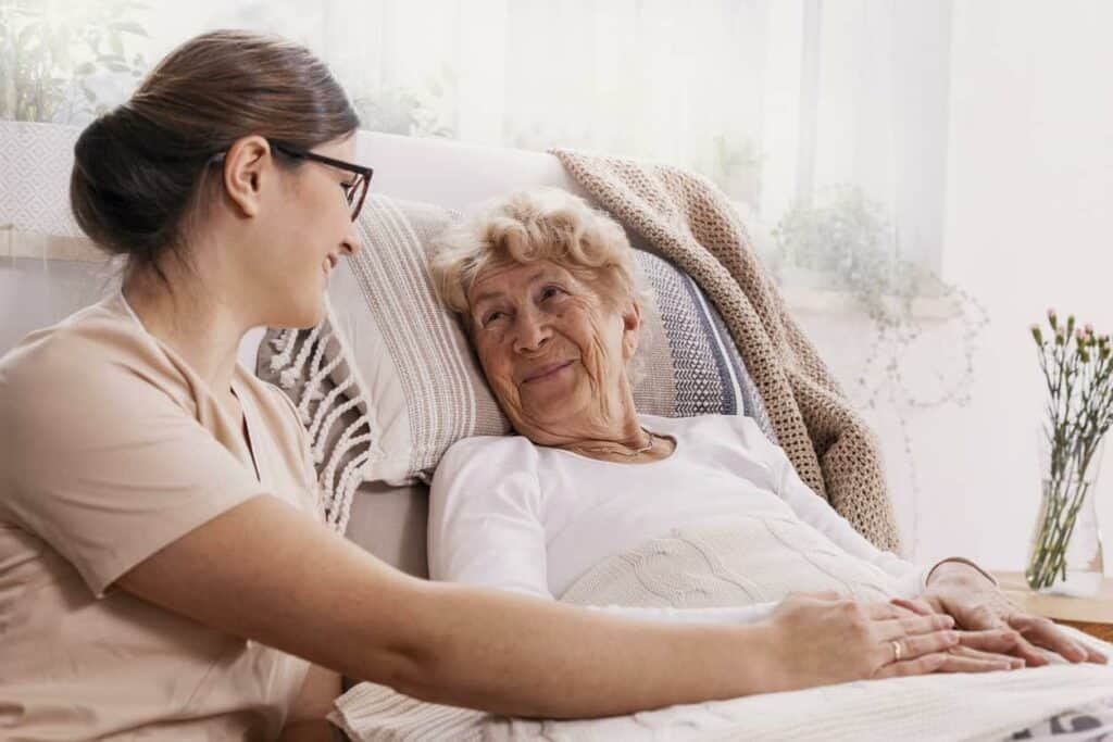 A senior woman in bed talking with her caregiver - dementia stages.