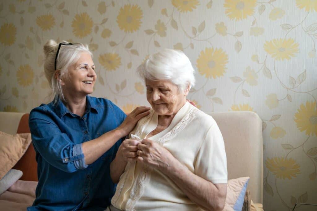 A senior woman with mild dementia assisted by a caregiver with dressing - dementia stages.
