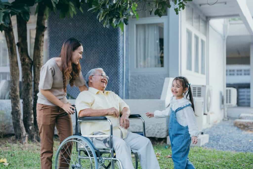 Elderly Asian man spending time with her grand-daughter and being supported by his female carer who was hired through a home health care service