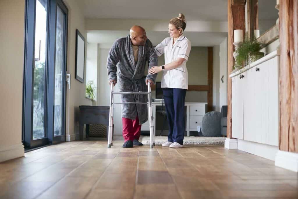 Black senior man using a walking frame and being assisted by his female caregiver from a home health care services in Reno, NV