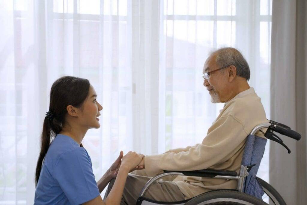 A caregiver talking to an older man on a wheelchair - hoyer lift chair.