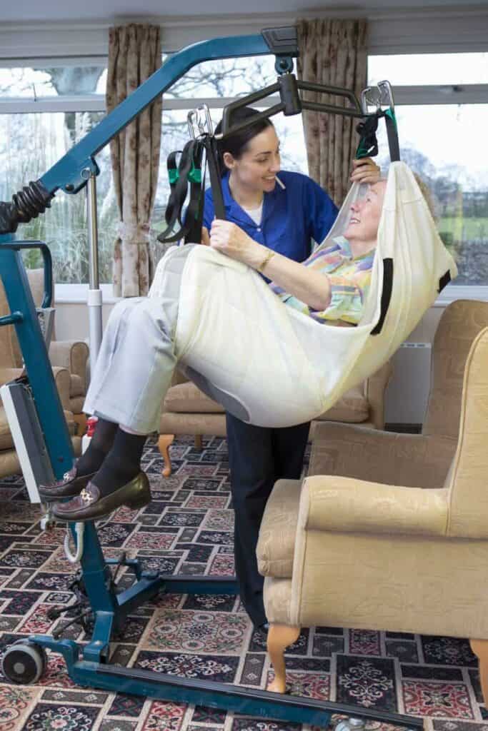 A caregiver and senior woman on a Hoyer lift.