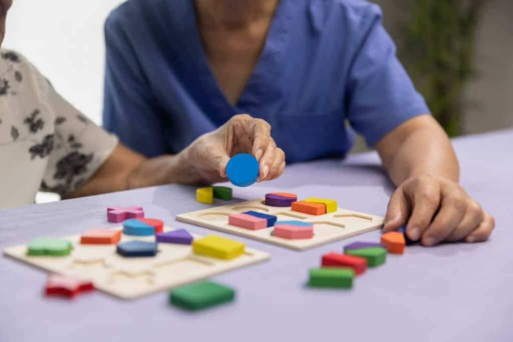Older person playing wooden puzzle game with caregiver- what are the 7 stages of dementia