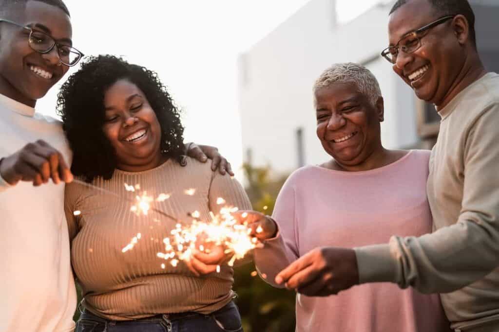 Black elderly woman lighting sparklers with her family at an assisted living home’s garden