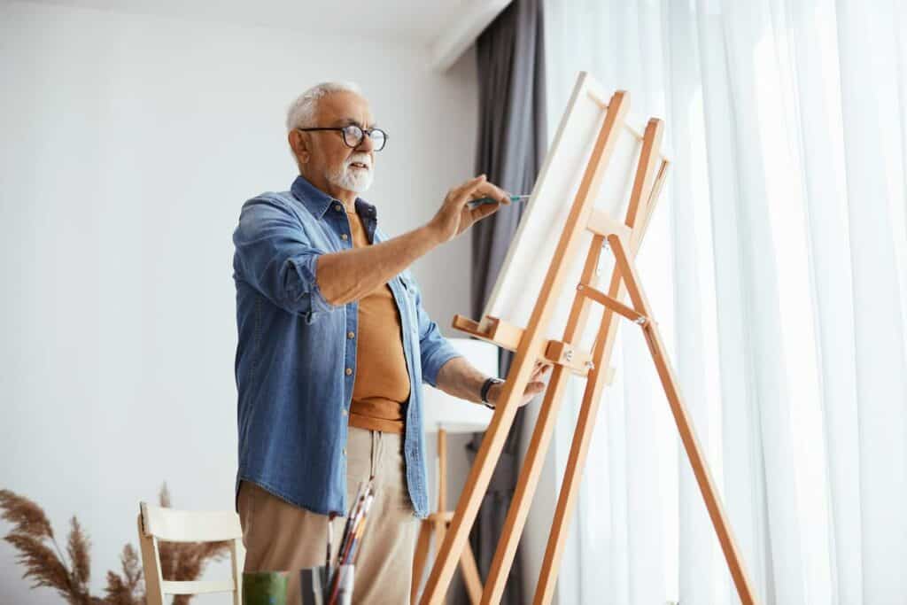 Elderly man standing up and painting on a canvas at a senior assisted living facility
