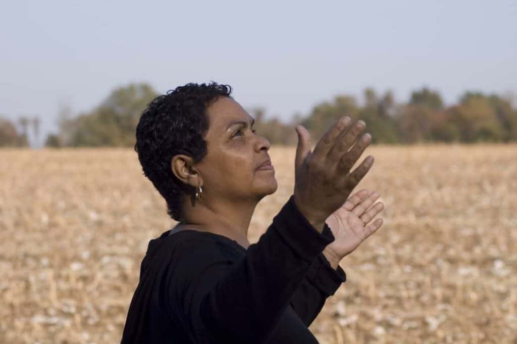Black woman on an open field raising her hands and thanking for being alive | when you see a dragonfly meaning
