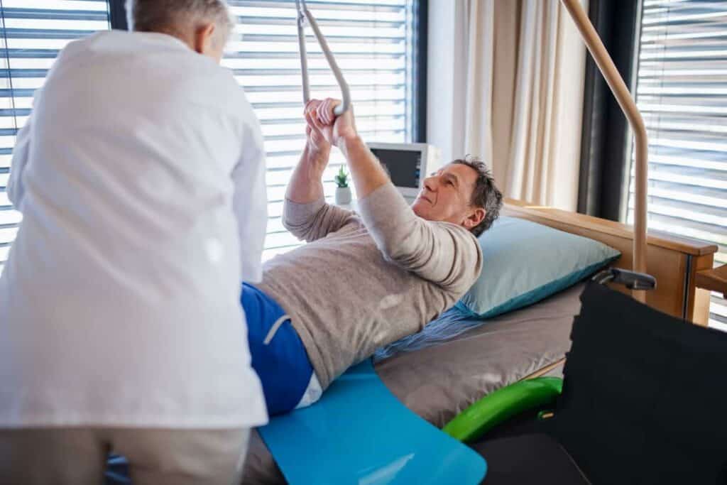 A caregiver helping a senior man to move from bed to a wheelchair - hoyer lift sling types.