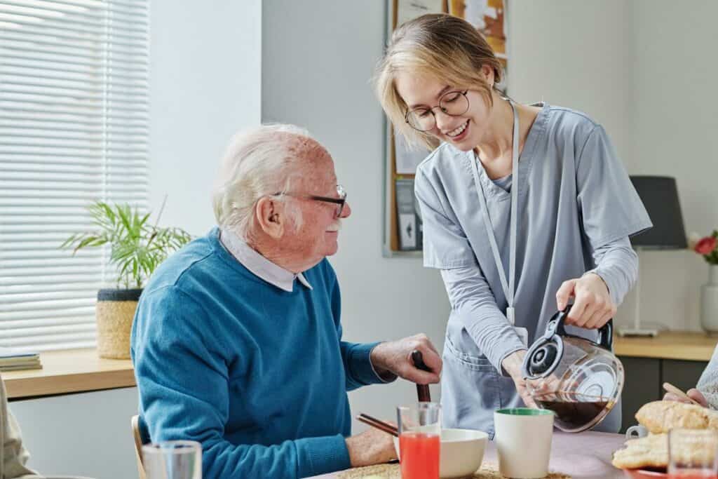 residential assisted living facility - caregiver pouring coffee for elderly man