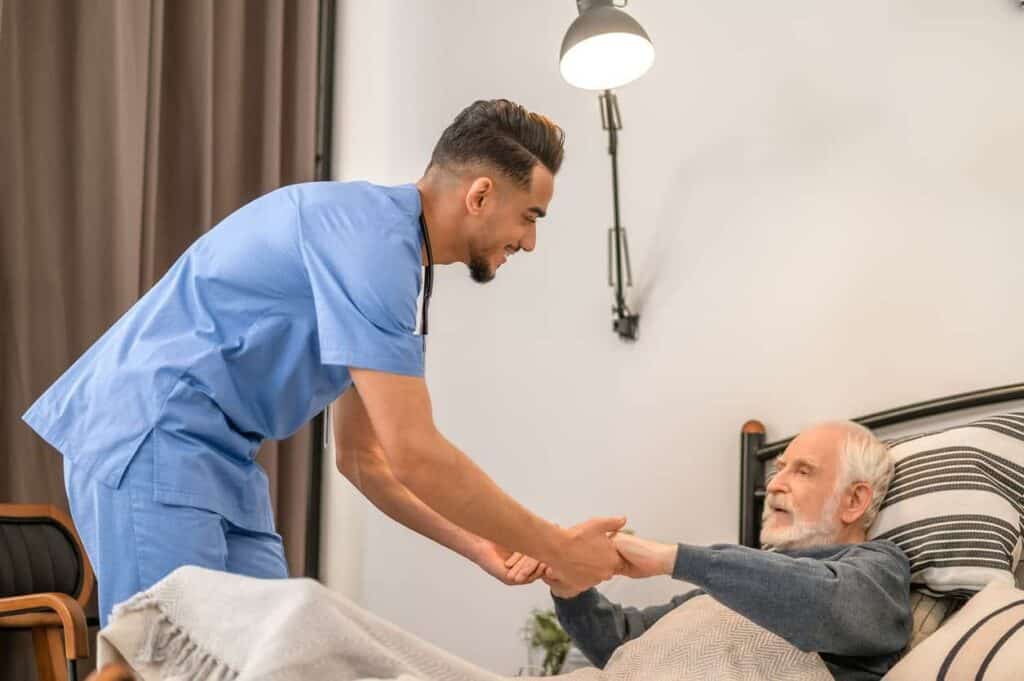 Hoyer lift electric - a male caregiver preparing a senior man in bed for a transfer.