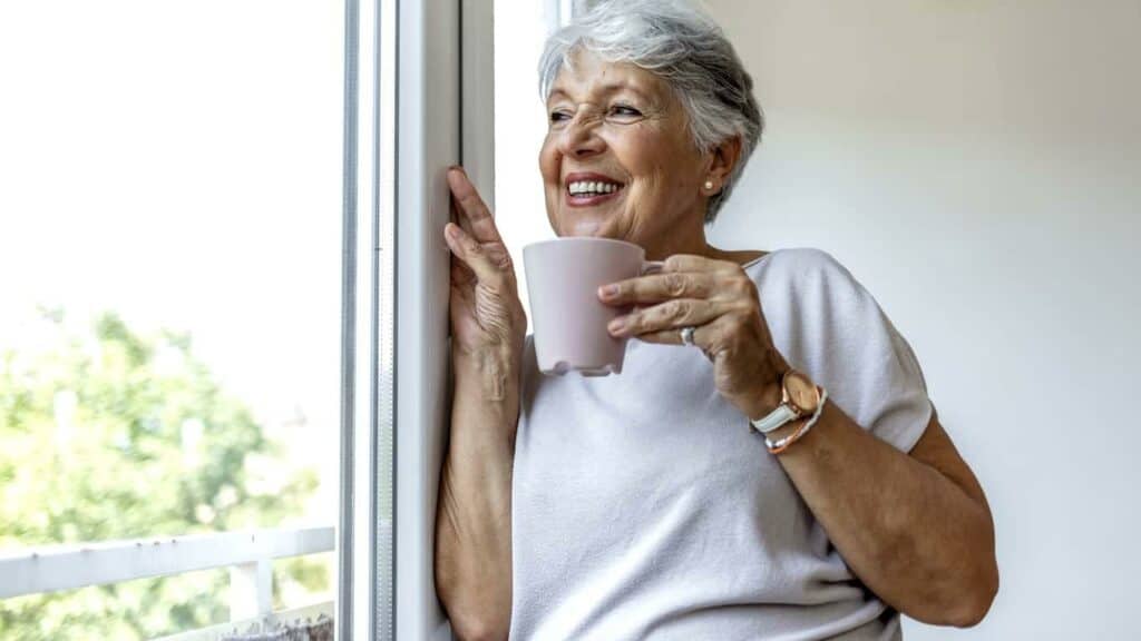 an older woman enjoying a cup of tea as she watches the beautiful view from her apartment assisted living