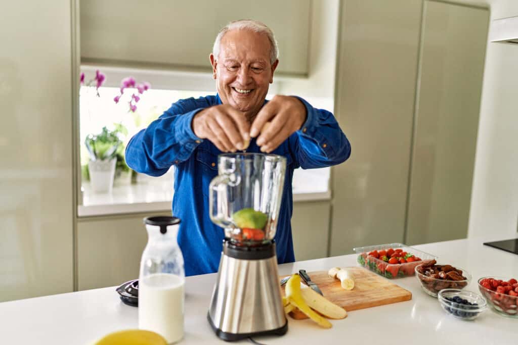 Elderly man making a smoothie with ensure powder and fruits - ensure milk benefits for adults