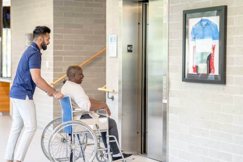 a male caregiver pushing a senior woman on a wheelchair - compact Hoyer lift