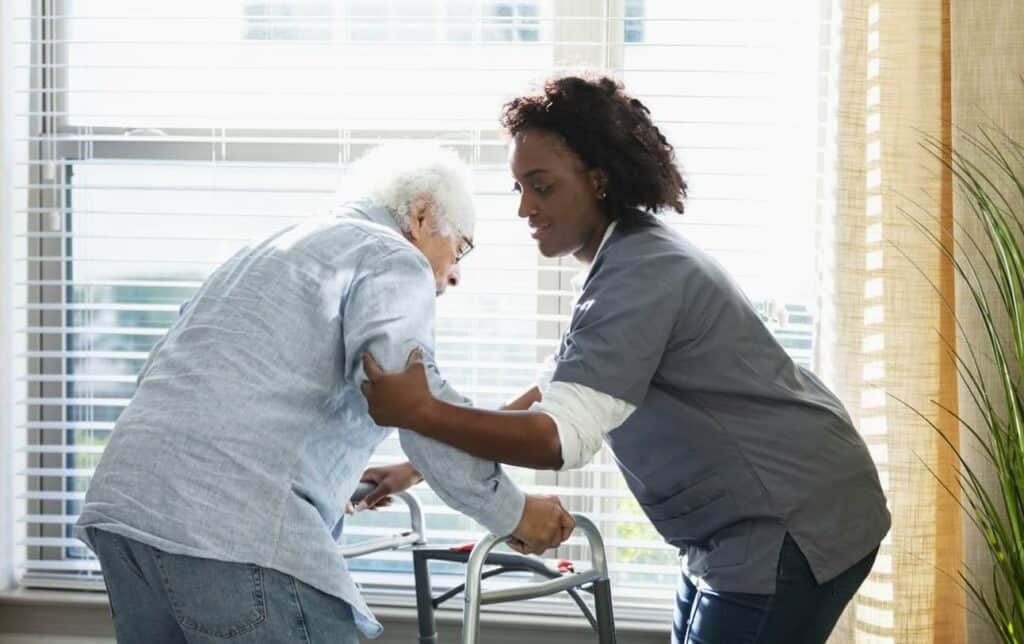 a caregiver supporting a senior man on a walker - mini Hoyer lift