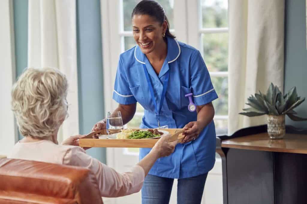 Female care worker bringing a meal to a senior woman in an assisted living home in Indian Hills, NV