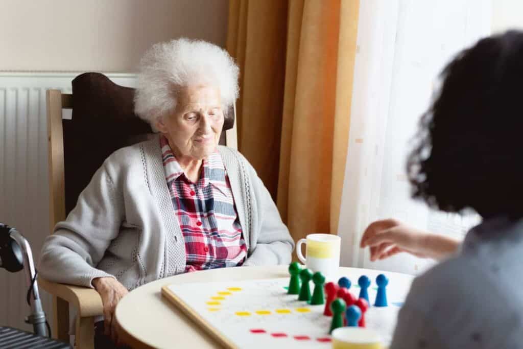 A senior woman playing a board game with her caregiver - caregiver job description.