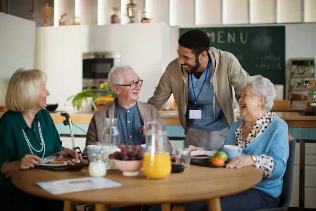 Senior caregiver laughing while enjoying breakfast with three seniors - Senior Care Jobs in Reno NV