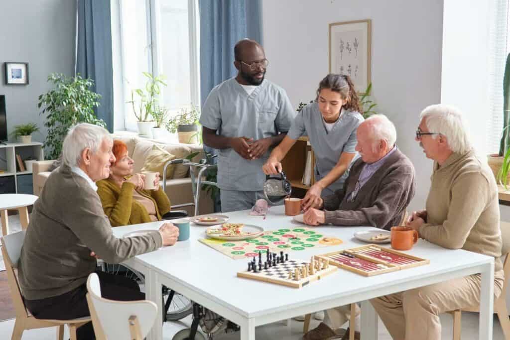 Caregiver is pouring tea while seniors are sitting around the table - senior living