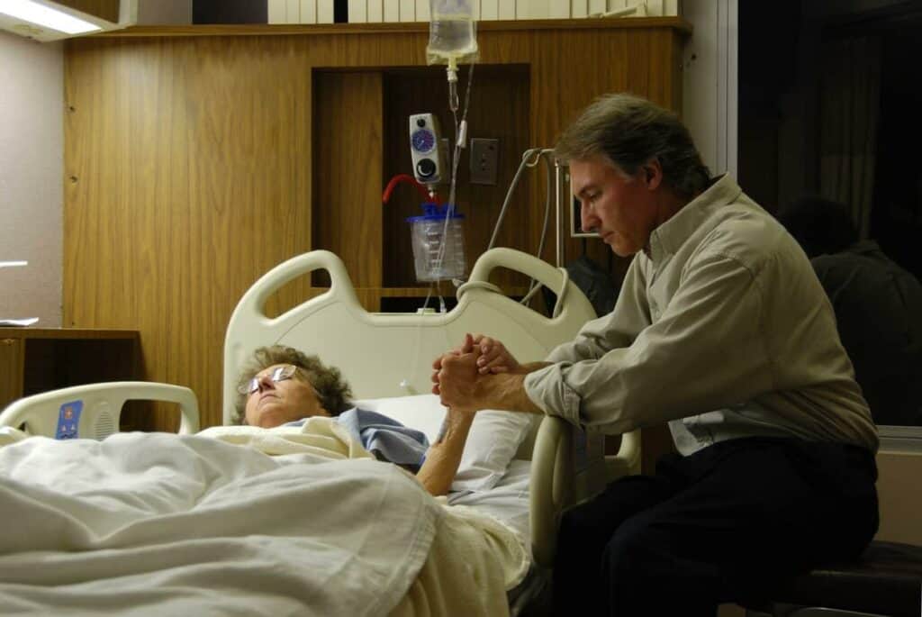 chaplain praying with an elderly woman in a hospice facility