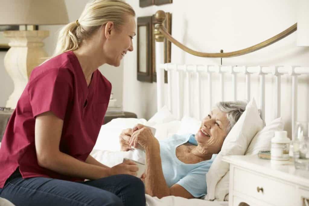 A volunteer talking to a woman patient lying in bed.